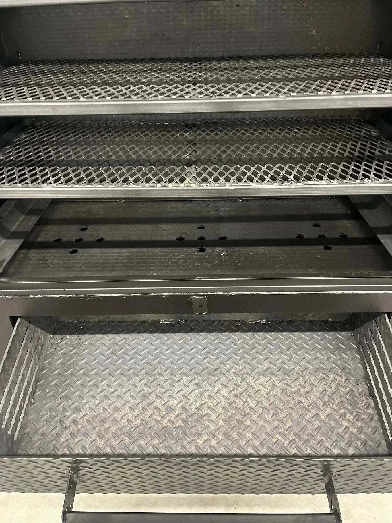Interior view of the SNS 42 Cabinet Combo Smoker showing multiple steel racks and a diamond plate bottom tray for wood or charcoal smoking.