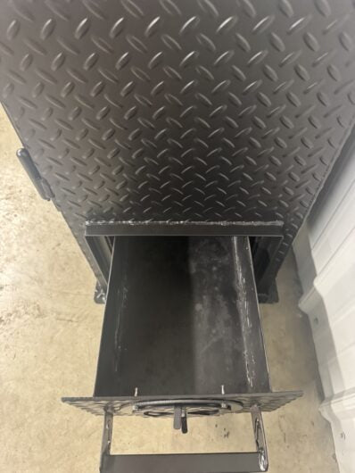 Metal grill with open ash drawer on a textured surface