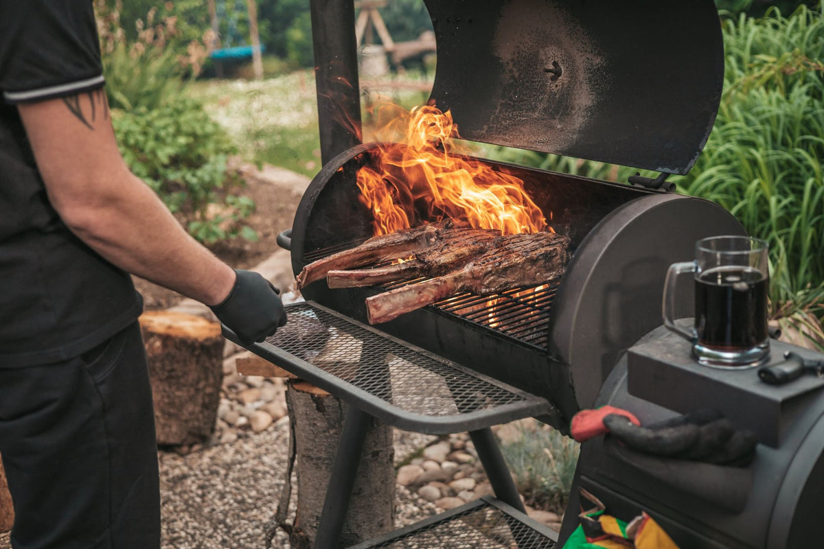 Pitmaster grilling tomahawk steaks over open flames on an offset barrel smoker in a backyard