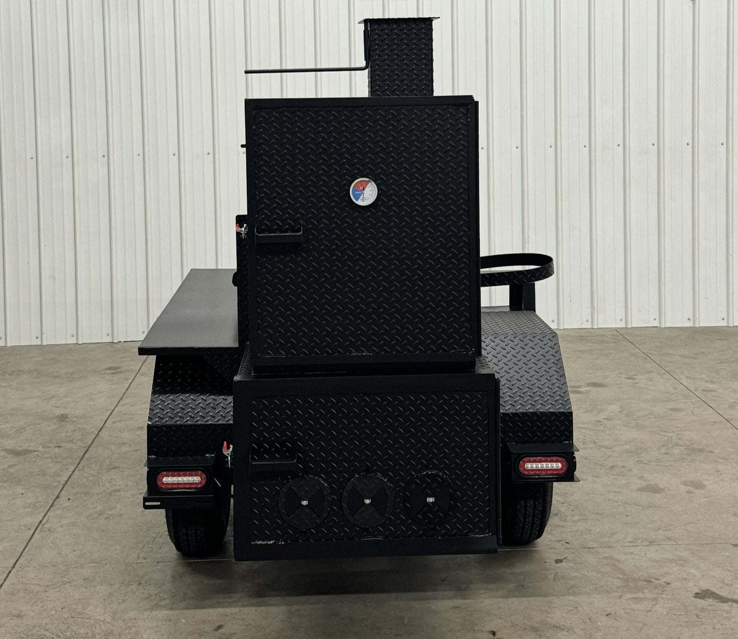 Black Competition 60 barbeque smoker with insulated firebox and rib box on wheels against white wall