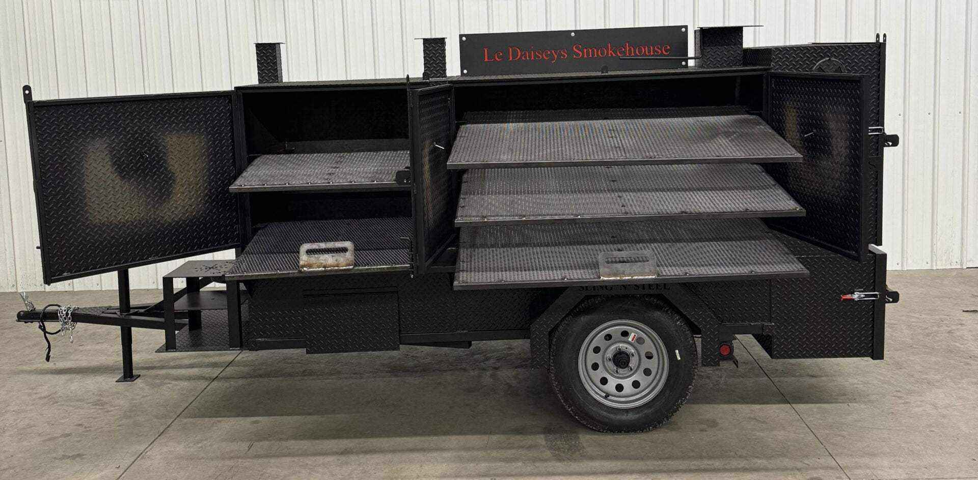 Custom charcoal grill trailer with multiple smoking racks and side compartments for catering use
