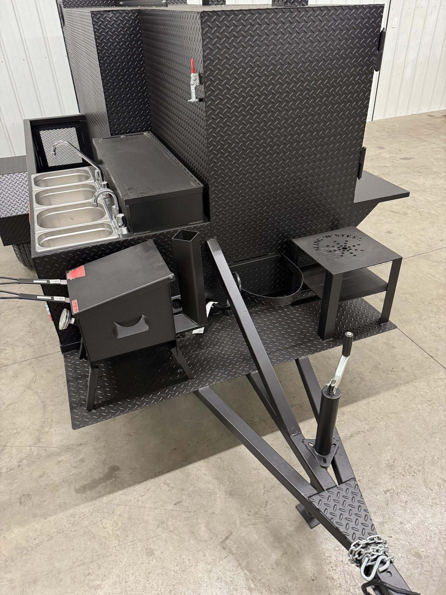 Custom black charcoal grill and SNS 4060 smoker trailer with multiple cooking compartments and prep stations designed for versatile catering and restaurant use