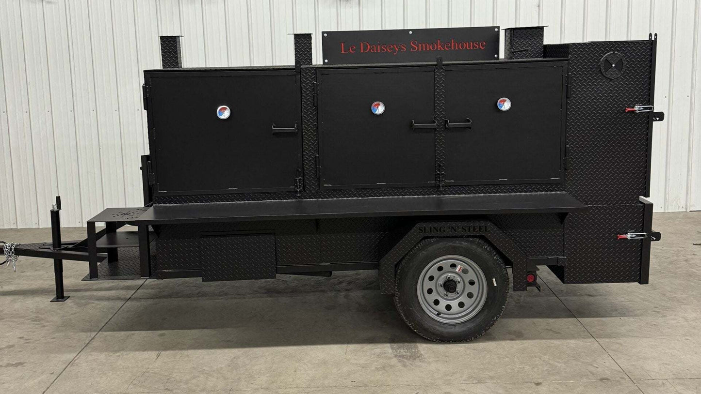 Custom charcoal grill and smoker trailer for catering with three cooking chambers and temperature gauges.