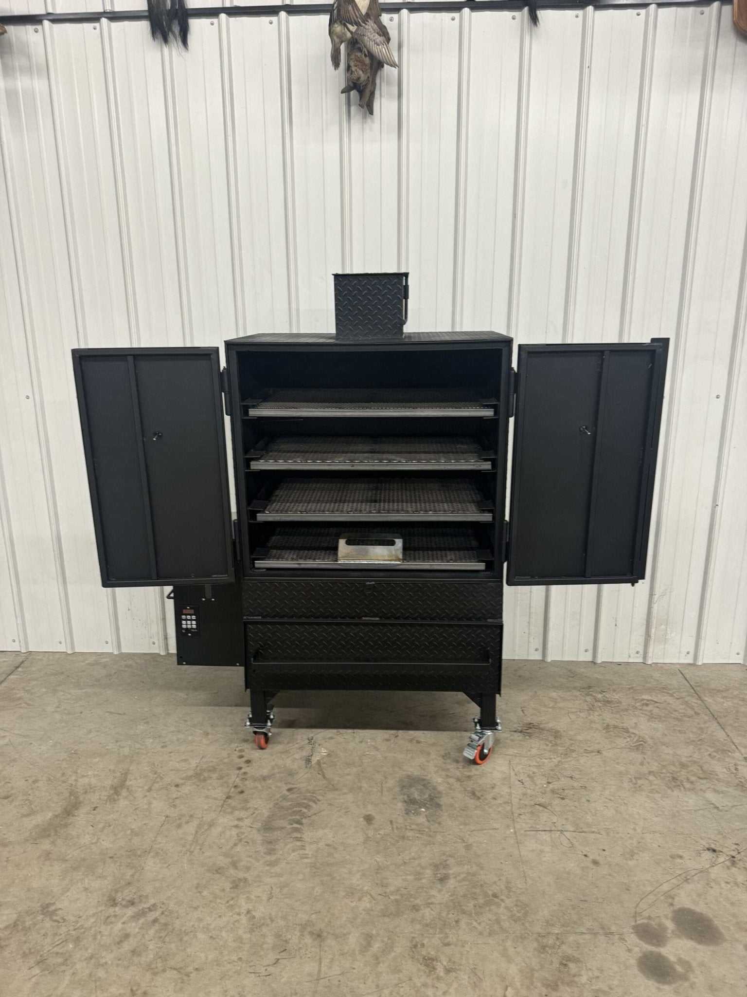 Commercial grade SNS Pellet Vault pellet smoker with open doors showing multiple slide-out cooking racks and grease pan inside, black steel construction, heavy-duty design for catering or backyard use