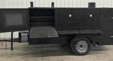 SNS 4060 Cabinet Smoker with charcoal grill, multiple cooking racks, insulated firebox, and storage basket on trailer.