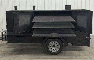 SNS 4060 smoker grill with cabinet main chamber, three slide-out cooking racks, mounted on trailer with tire, black steel construction