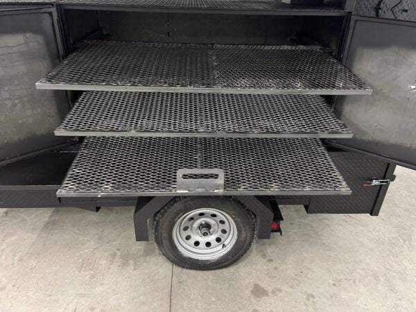 SNS 60 Cabinet Smoker showing open smoker with three slide-out cooking racks above a trailer wheel