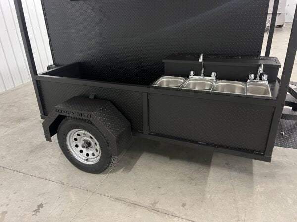 Commercial black smoker cabinet trailer with stainless steel sink and fold-down roof package for BBQ catering and grilling.