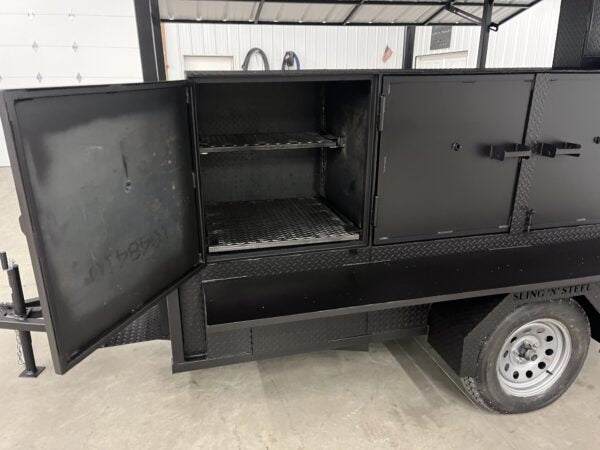 Black SNS 60 smoker cabinet trailer with open door showing interior cooking racks and wheels