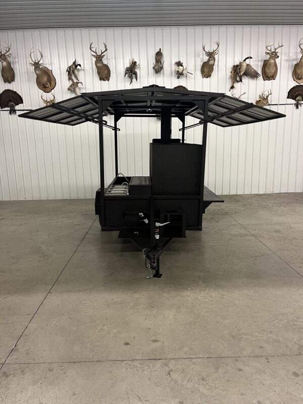 Commercial smoker cabinet and grill combo with fold-down roof, sink, and storage basket on trailer.