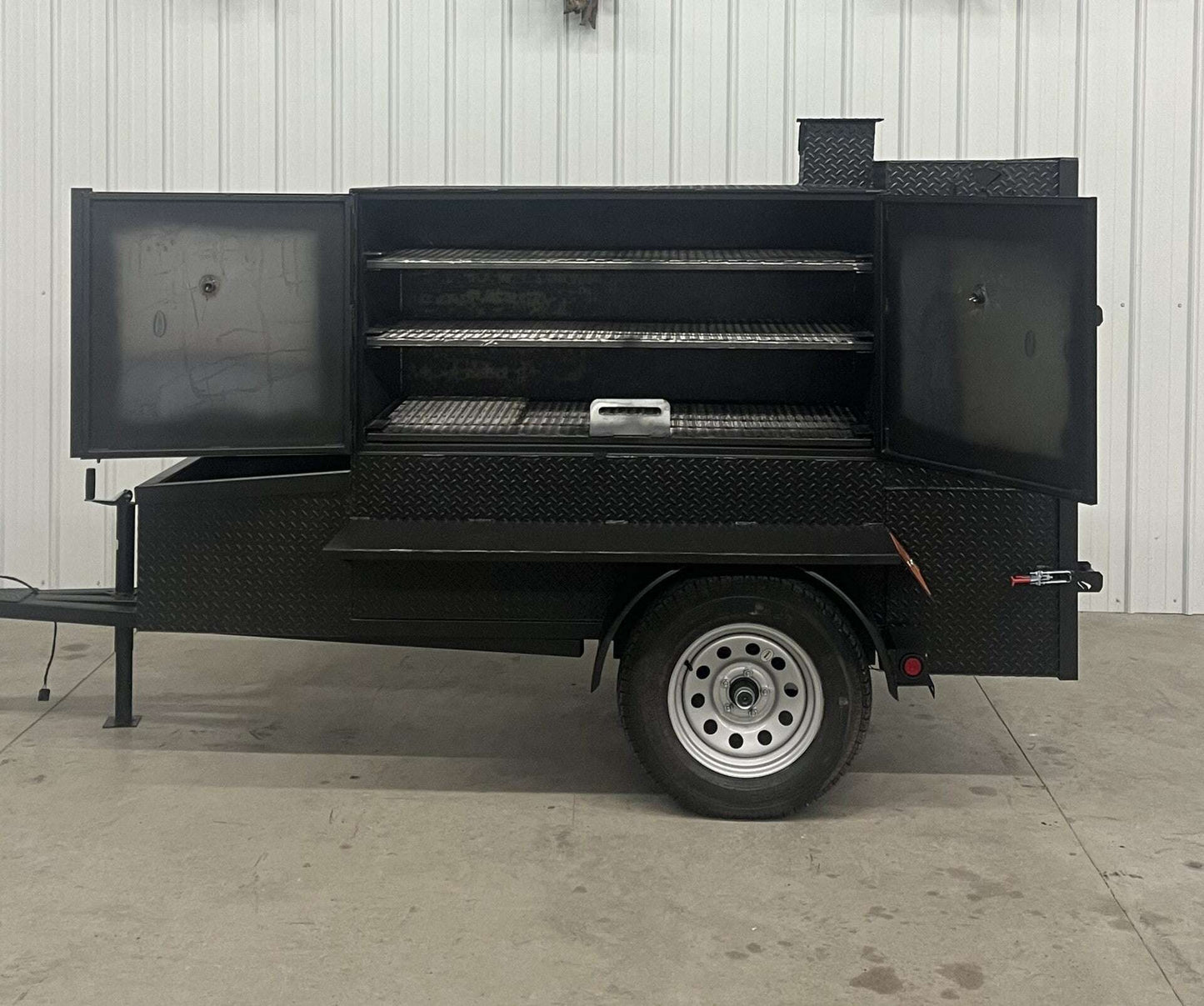SNS 60 Cabinet Trailer Smoker with open doors showing three slide-out cooking racks and insulated firebox on a single axle trailer.