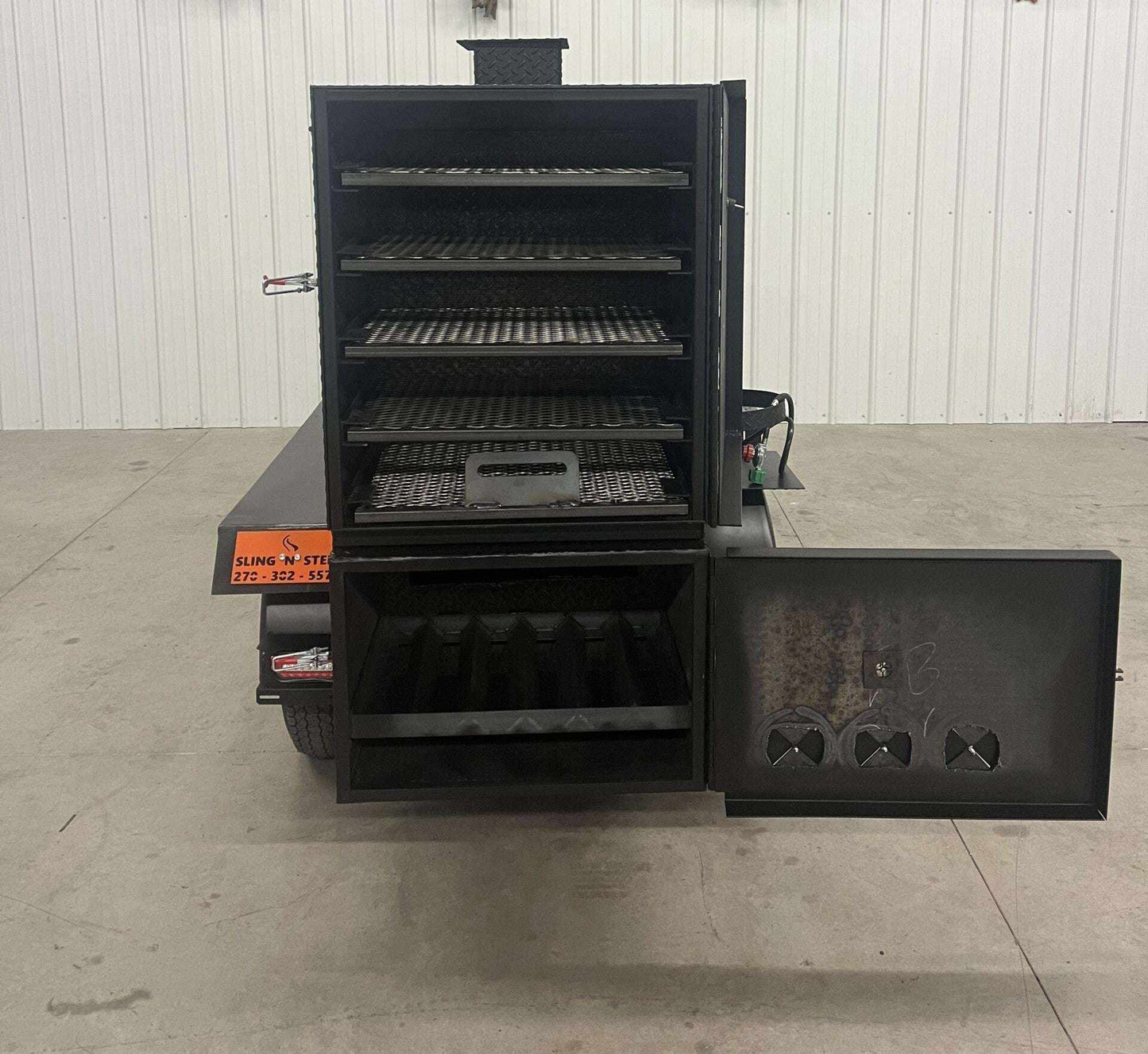 SNS 60 smoker cabinet trailer with open door showing multiple slide-out cooking racks and insulated firebox compartments