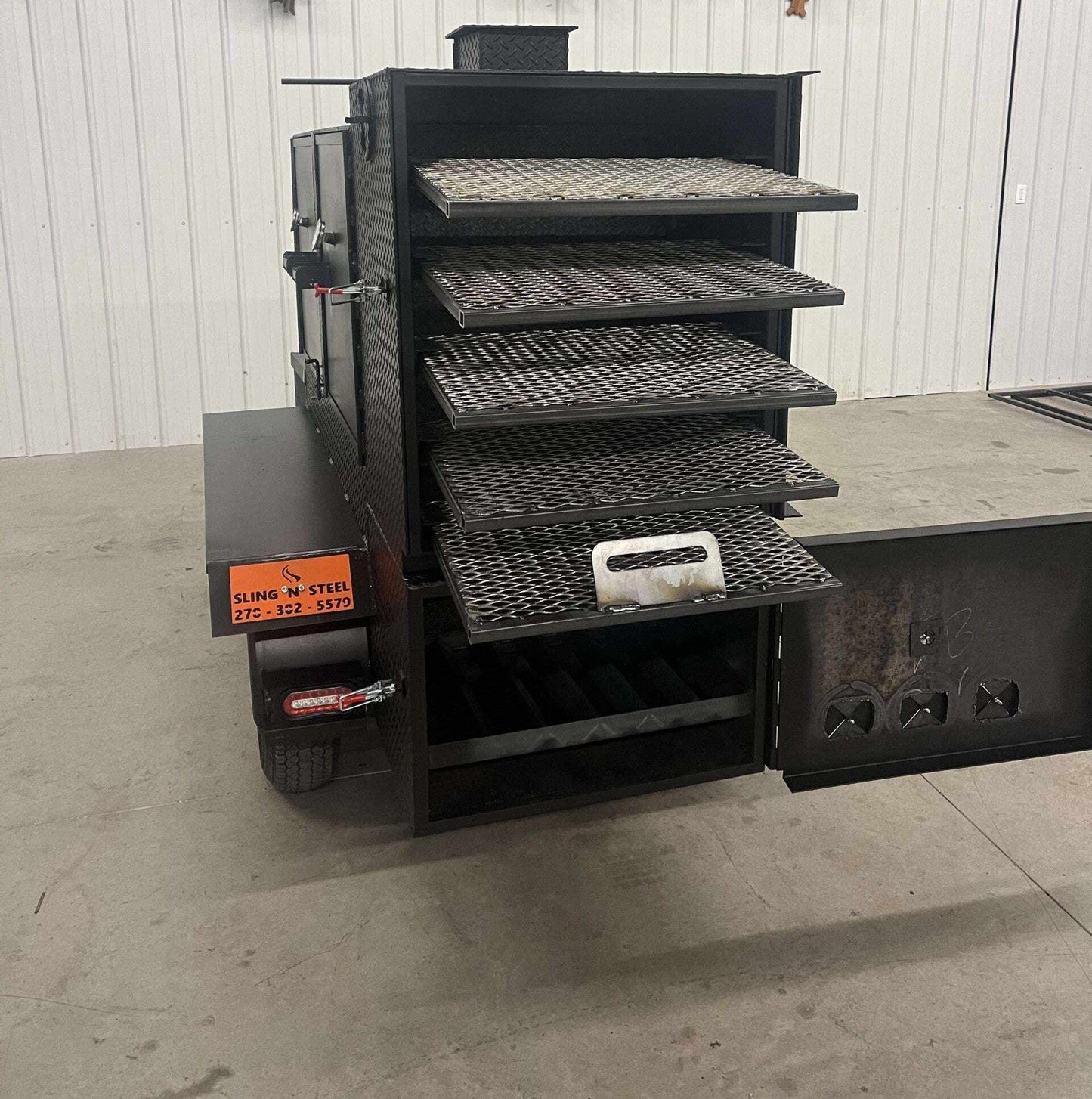 SNS 60 Smoker cabinet trailer with four slide out cooking racks and insulated firebox, heavy-duty steel construction.