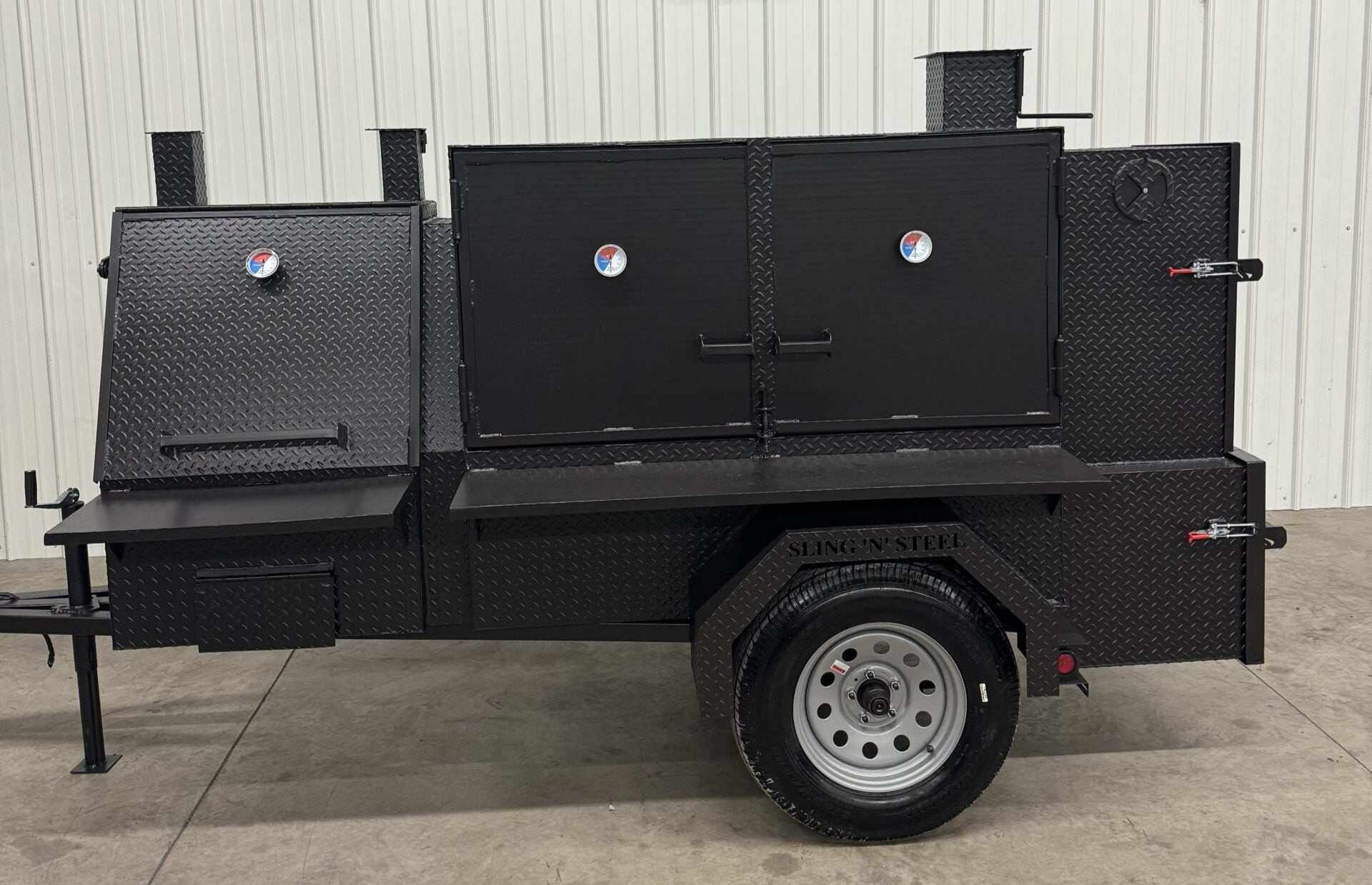 Black Smoker and Grill SNS 60 Cabinet mounted on trailer with multiple doors and temperature gauges in a warehouse setting