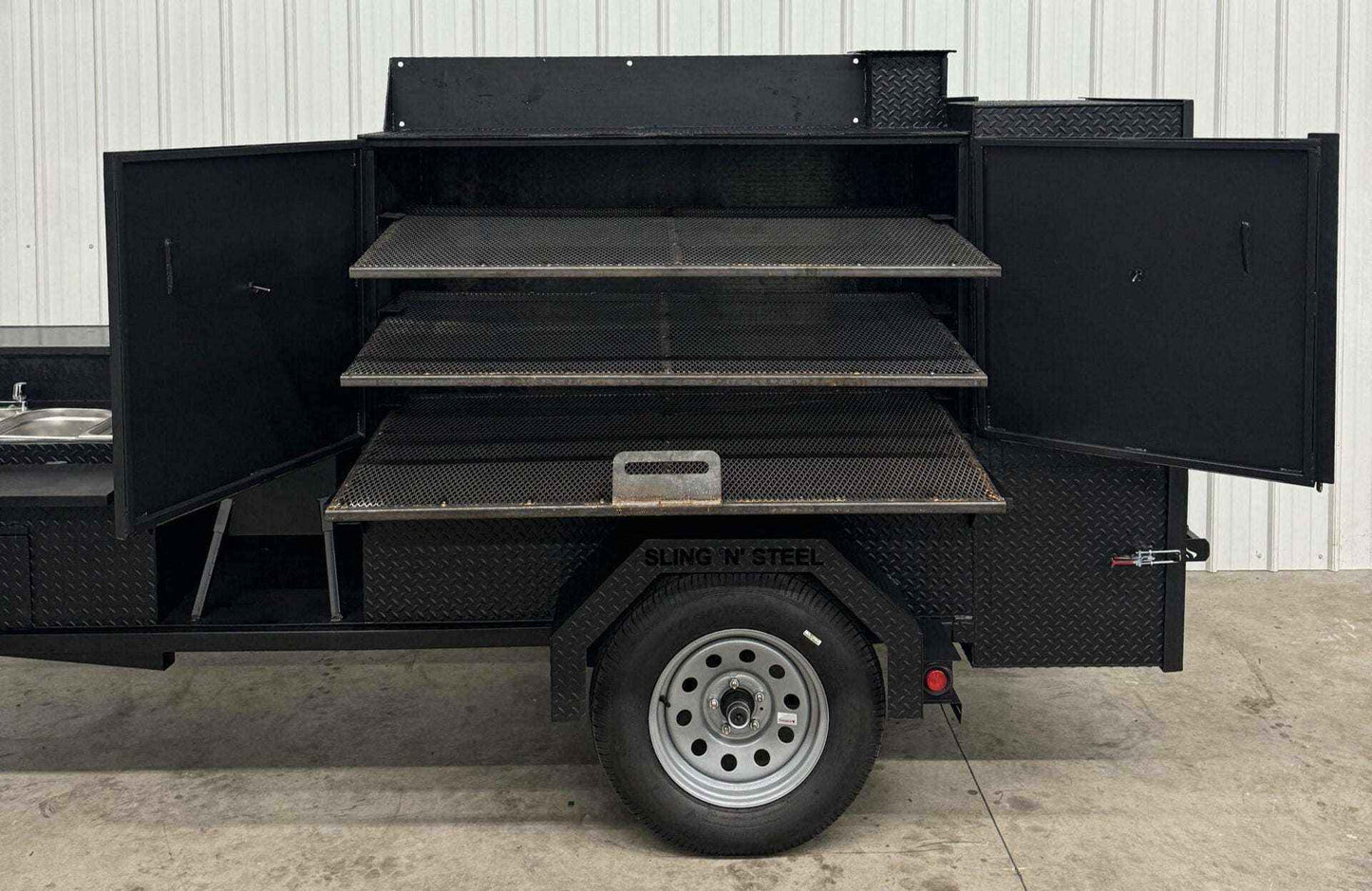 SNS 60 Cabinet reverse flow smoker with three slide-out cooking racks, insulated firebox, rib box, sink package, and deep fryer mounted on trailer with diamond tread steel body