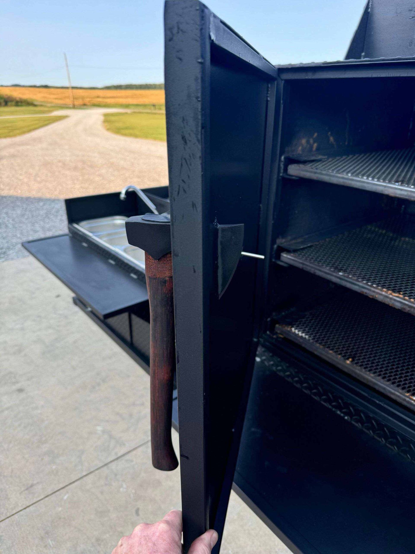 SNS 60 cabinet smoker with open door showing multiple cooking racks and a built-in sink package outdoors on concrete surface