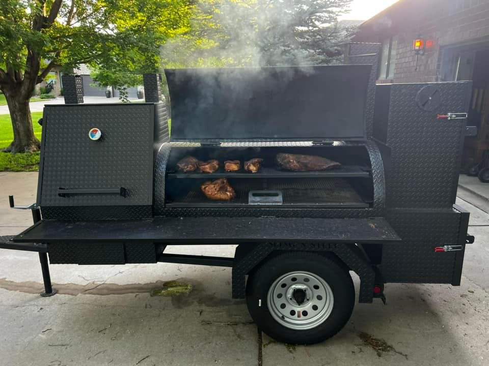 60-inch SNS Barrel smoker and charcoal grill trailer with adjustable smoke stacks and multiple cooking racks smoking meat outdoors