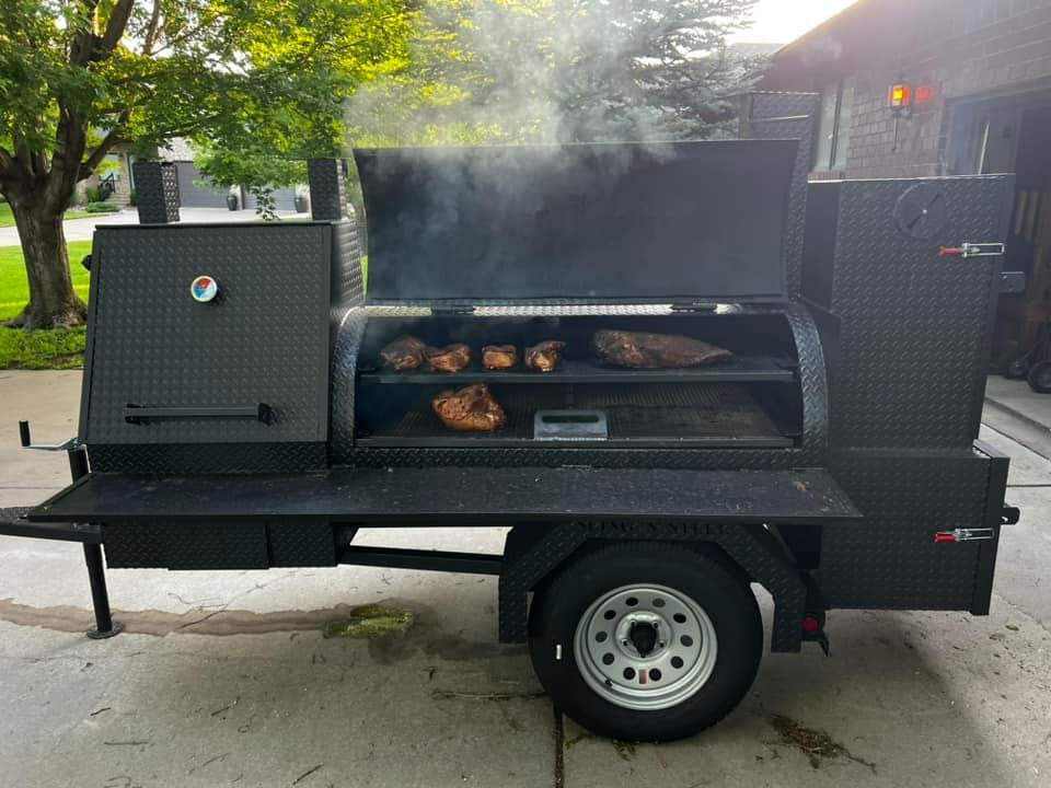 Large black SNS Barrel 60 reverse flow smoker and charcoal grill trailer with smoking meat inside, featuring insulated firebox and rib warming box, ideal for catering businesses.