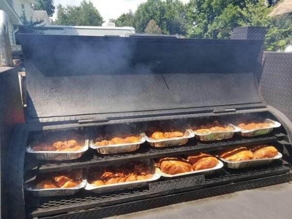 SNS Barrel 60 reverse flow smoker with two cooking racks full of smoked chicken trays and visible smoke