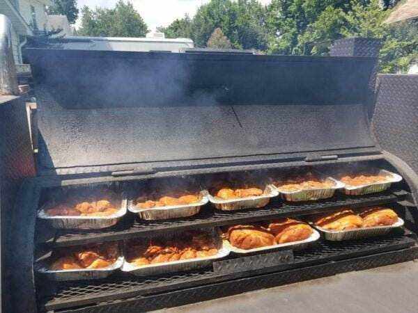 SNS Barrel 60 smoker with charcoal grill cooking multiple trays of meat with smoke rising outdoors