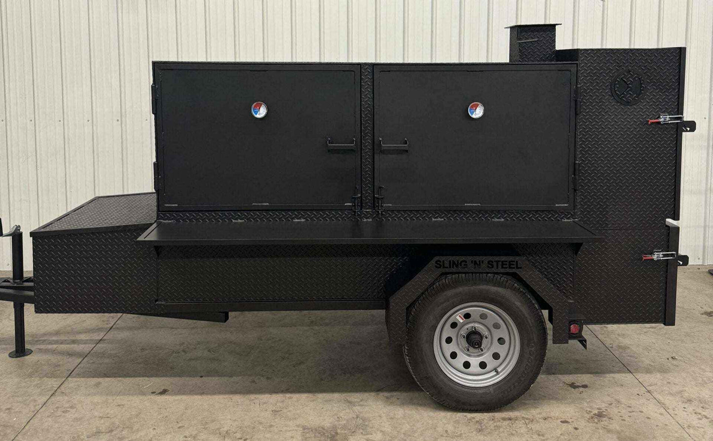 Large black SNS Beast box smoker cabinet on trailer with dual doors and firebox against white metal wall