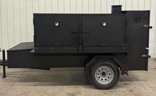 Large black SNS Beast box smoker cabinet on trailer with dual doors and firebox against white metal wall