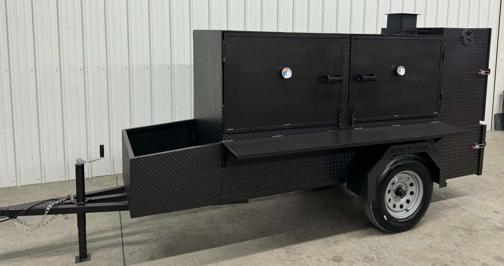 Large black Box Smoker SNS Beast cabinet smoker with diamond tread steel construction and multiple cooking racks on trailer.