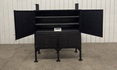 SNS Cabinet 60-inch concession charcoal grill with open cabinet doors on a concrete floor against a metal wall