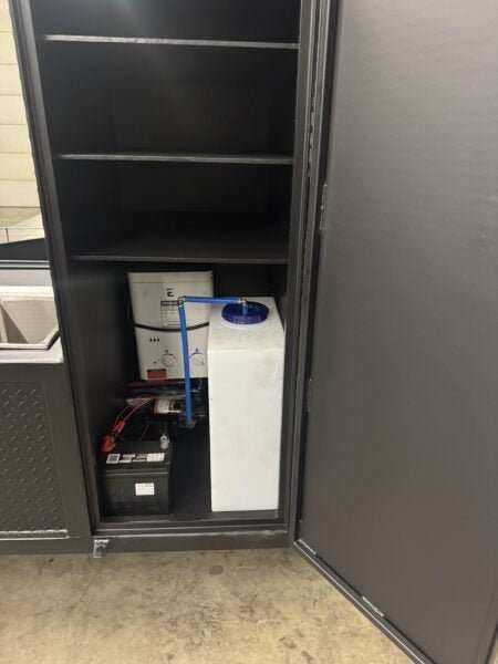 SNS Hospitality Trailer storage compartment with battery and water container inside black metal cabinet