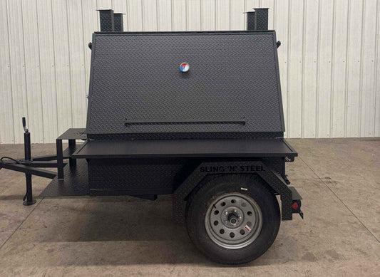SNS Mega Grill black mobile grilling trailer with dual cooking pits and pull-out charcoal trays on a single axle trailer