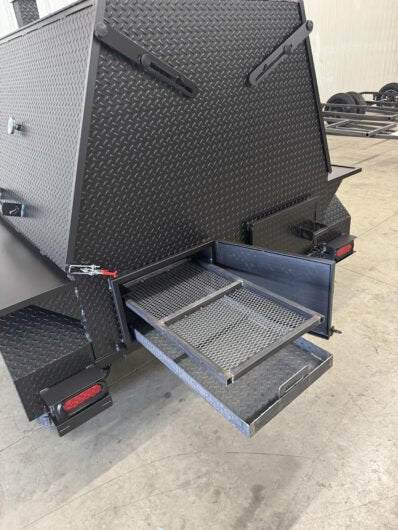 Black SNS Mega Grill grilling trailer with pull-out charcoal tray and ash pan open for grilling.