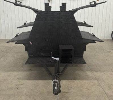SNS Mega Grill black commercial grilling trailer with dual cooking pits and pull-out charcoal trays in indoor warehouse.
