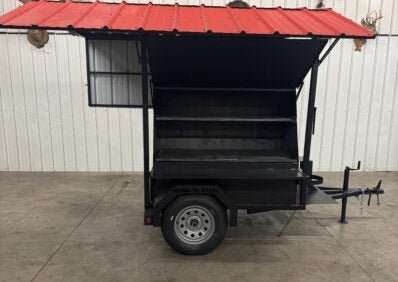 Black SNS Mega Giant Grill trailer with roof and dual cooking pits on single axle in warehouse setting