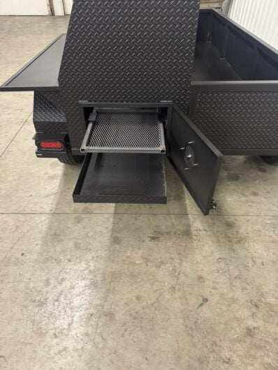 SNS Pellet Vault and Charcoal Grill Combo with pull-out charcoal tray and ash pan in a black metal trailer.