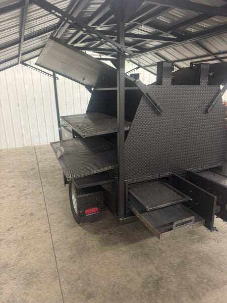 SNS Ultimate Mega Grill commercial charcoal grill trailer with two-sided main chamber, pull-out charcoal trays, rotating racks, and heavy-duty steel construction under roofed structure