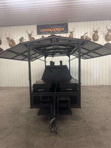 SNS Ultimate Mega Grill commercial charcoal grill trailer with two-sided grill chamber, pull-out charcoal trays, ash pans, rotating stainless steel racks, and roof package in indoor setting.