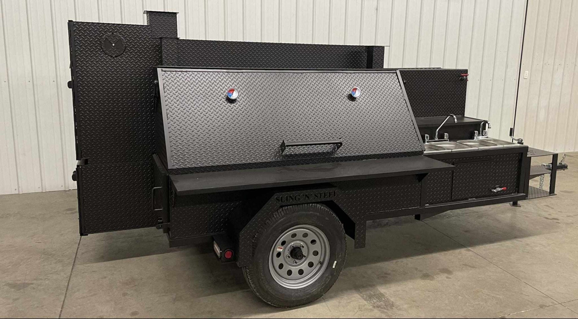 SNS Ultimate Smokehouse 60-inch charcoal smoker with sink, griddle, and triple cooking racks on a trailer