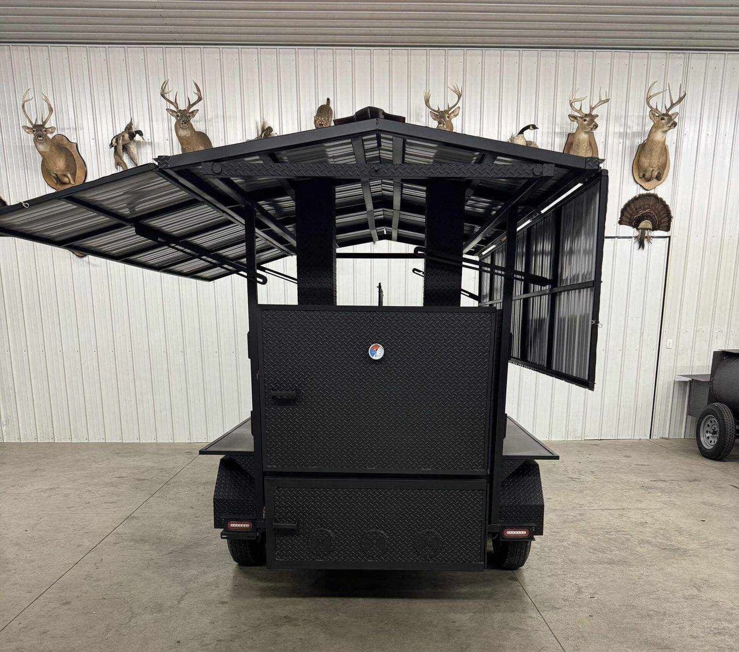 Commercial Smoker Avery large black commercial smoker with open side panels in indoor setting with mounted deer heads on wall