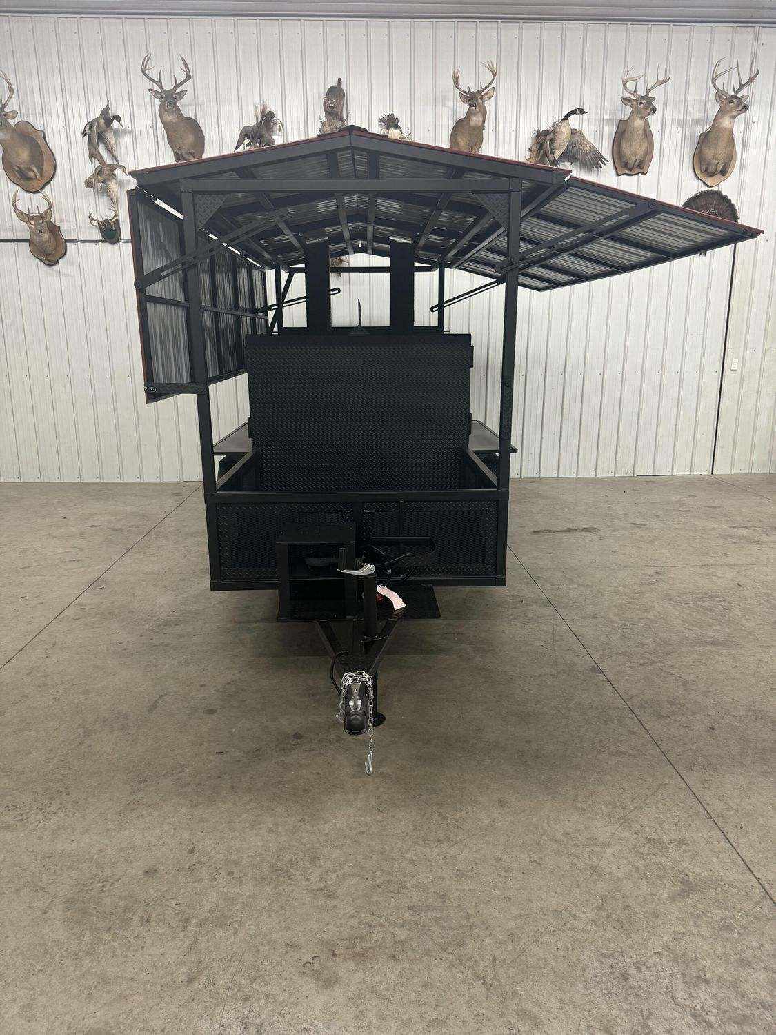 front view of large black Commercial Smoker Avery with open roof and trailer hitch in indoor space with mounted animal heads on wall