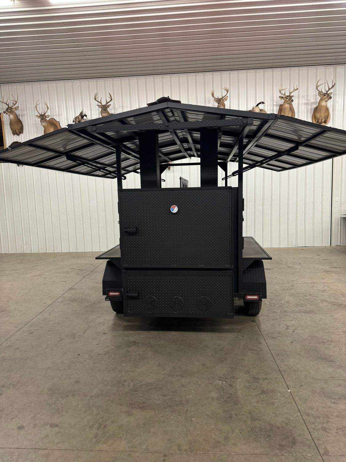 Commercial Smoker Avery large black commercial smoker with extended roof and trailer wheels in indoor setting