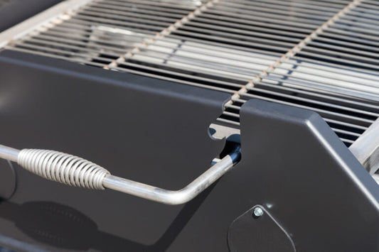 Close-up of a grill with a metal handle and coiled hose.
