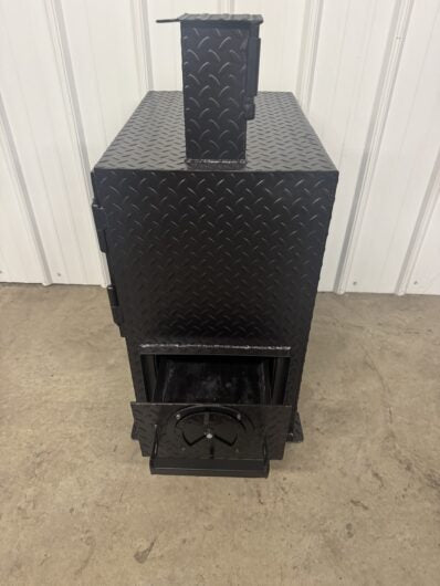 Black metal grill with diamond plate pattern on a concrete floor against a white wall.