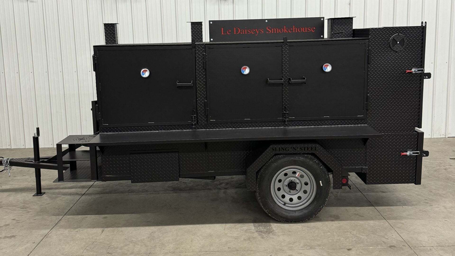 Custom charcoal grill and smoker trailer for catering with three cooking chambers and temperature gauges.