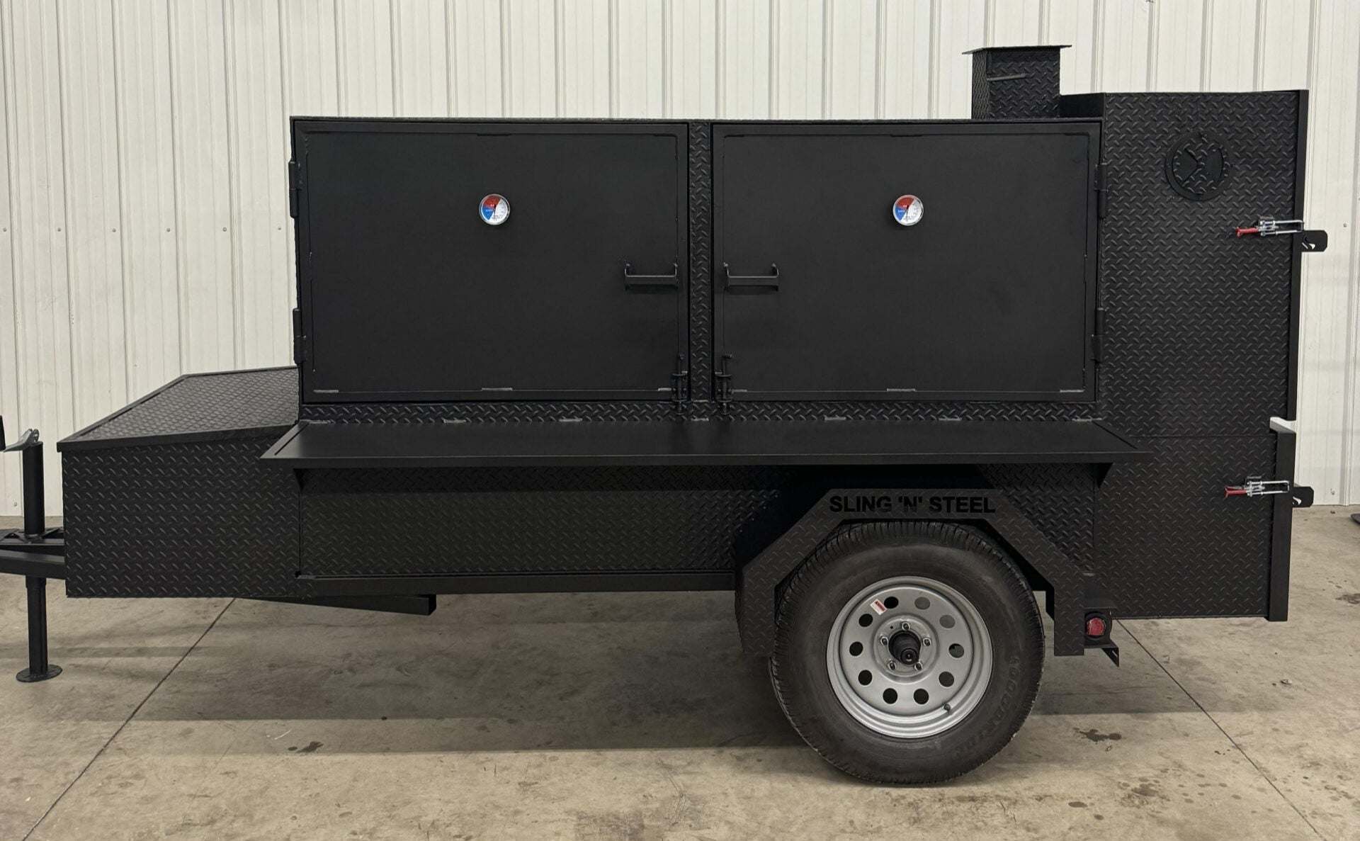 Black SNS Beast Cabinet Smoker with dual doors, diamond tread steel construction, mounted on trailer with single wheel, designed for large capacity barbecue cooking.