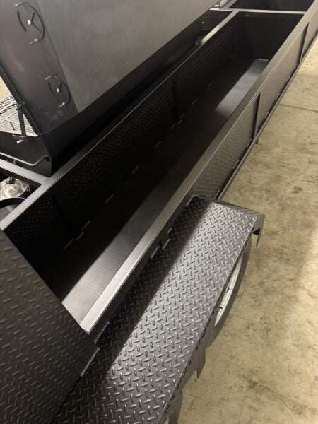 Black SNS Hospitality BBQ trailer with open cooking and storage compartments on a concrete floor.