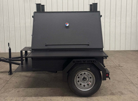 Compact black SNS Mega Grill portable grilling trailer with dual cooking pits and pull-out charcoal trays, designed for BBQ catering and outdoor cooking.